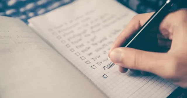 Persona comparando dos cursos en un portátil con una libreta y una lista de comprobación