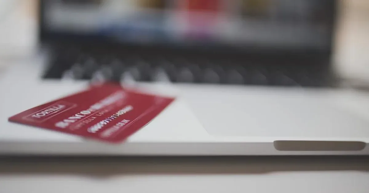 Persona revisando una compra online en el portátil con una tarjeta y un recibo sobre la mesa