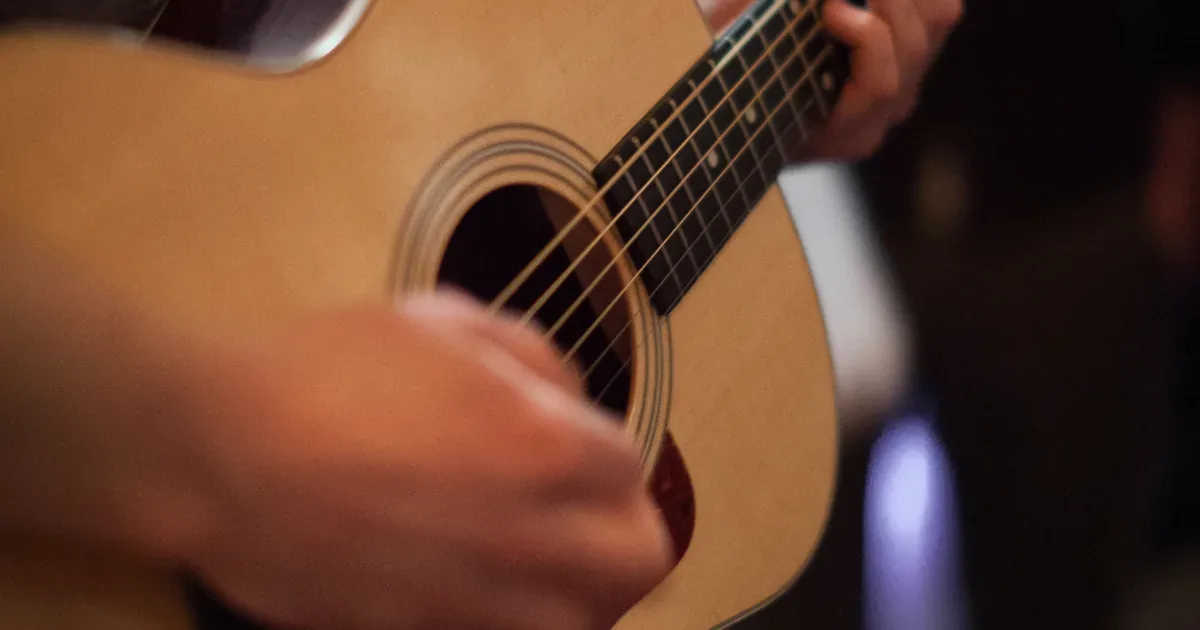 Persona principiante aprendiendo a tocar la guitarra acústica en casa con una tablet de apoyo