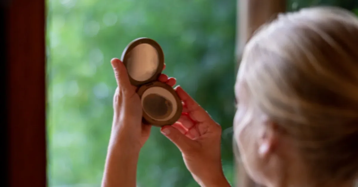 Mujer aplicándose maquillaje frente a un espejo con brochas y productos de belleza