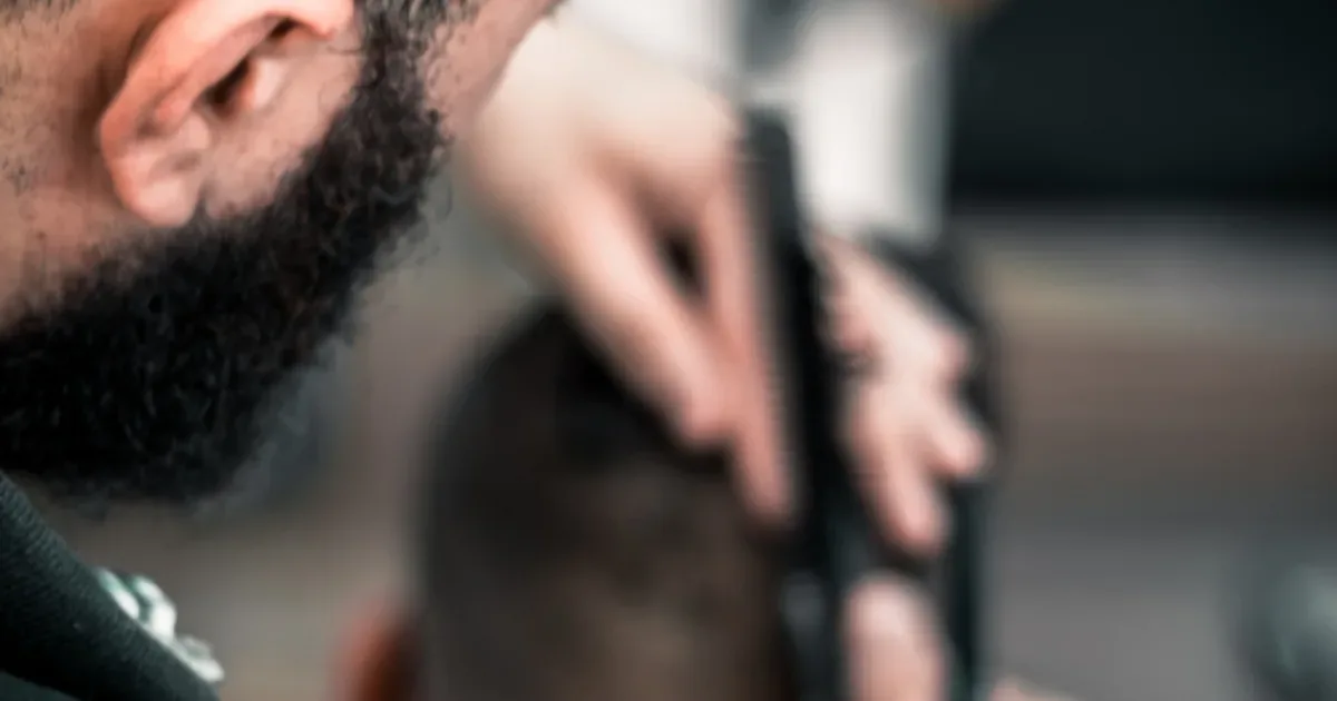 Barbero cortando el cabello a un cliente con tijera y peine en una barbería
