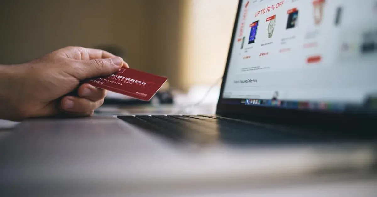Persona comprando un curso online desde un portátil con una tarjeta de pago junto al teclado
