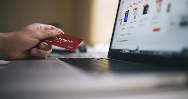 Persona comprando un curso online desde un portátil con una tarjeta de pago junto al teclado
